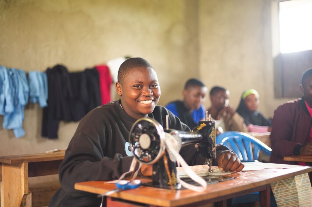 Mastering the First Impression: Your intriguing post title goes here Happy student in Uganda using sewing machine in class, highlighting education.